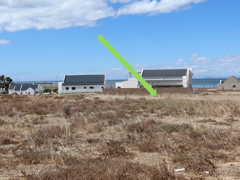 A view of a vacant residential plot of land with a boundary wall, situated in a coastal neighborhood.