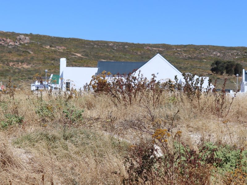 A view of a vacant residential plot featuring natural coastal vegetation with neighboring properties visible in the background.