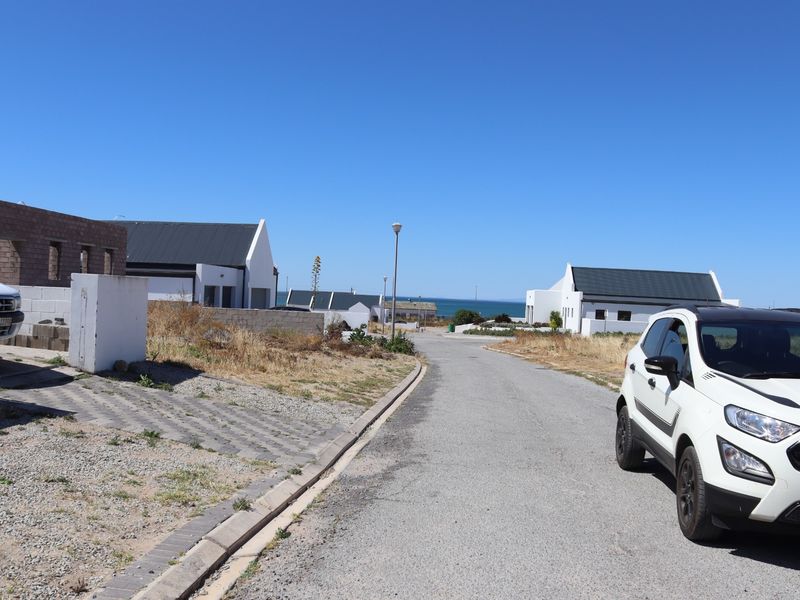 A street view of a residential development area featuring paved roads, concrete kerbing, and street lighting with distant ocean views.