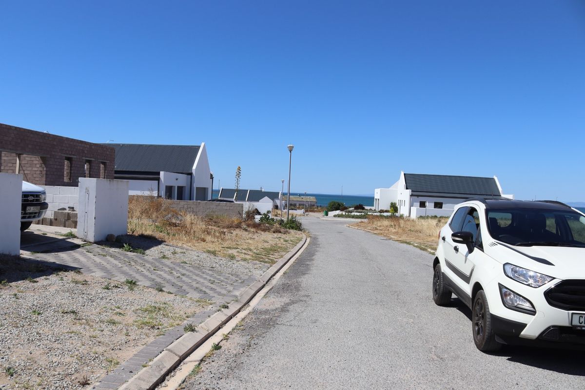 A street view of a residential development area featuring paved roads, concrete kerbing, and street lighting with distant ocean views.