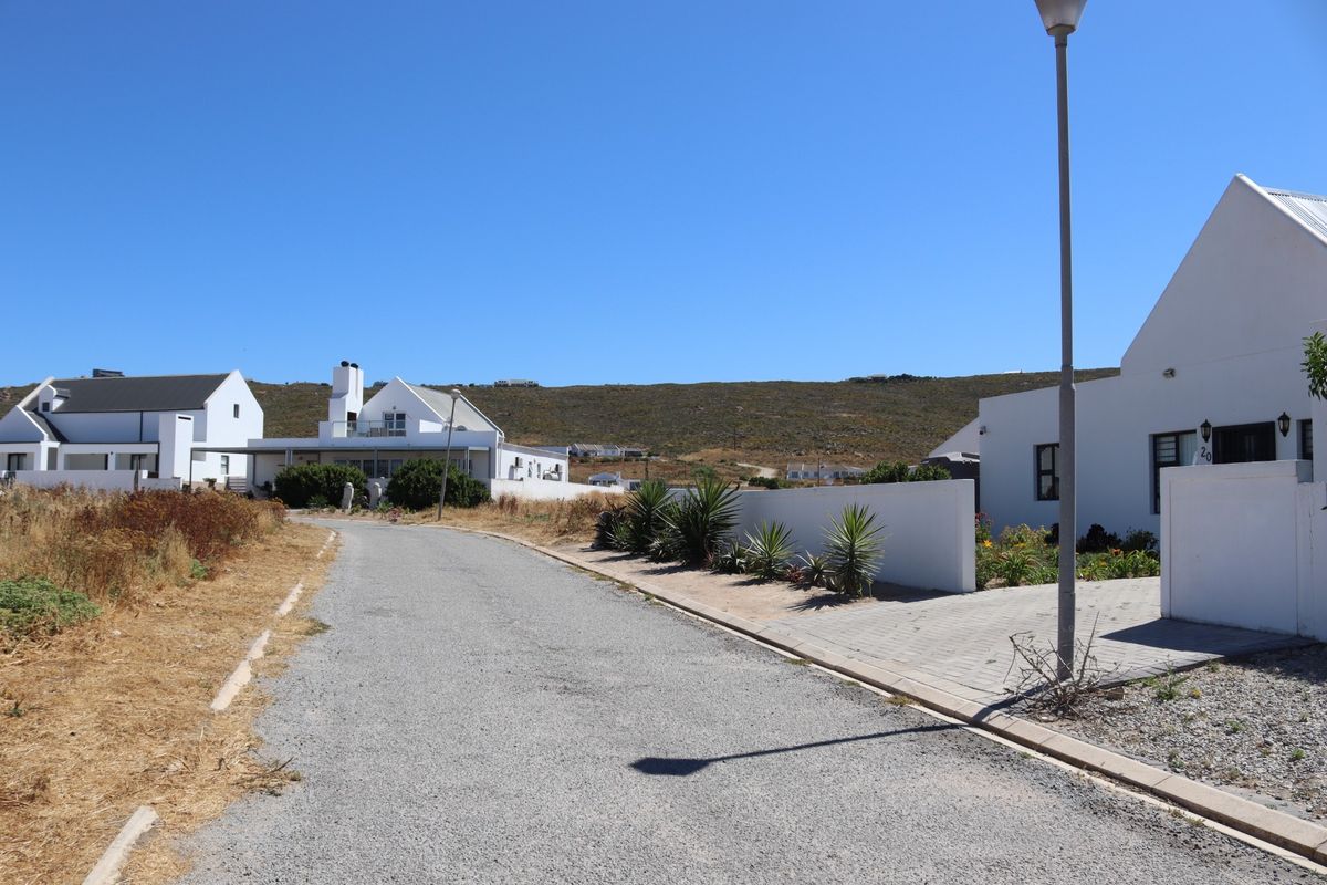 A view of the residential street showing paved road access, street lighting, and surrounding properties with boundary walls.