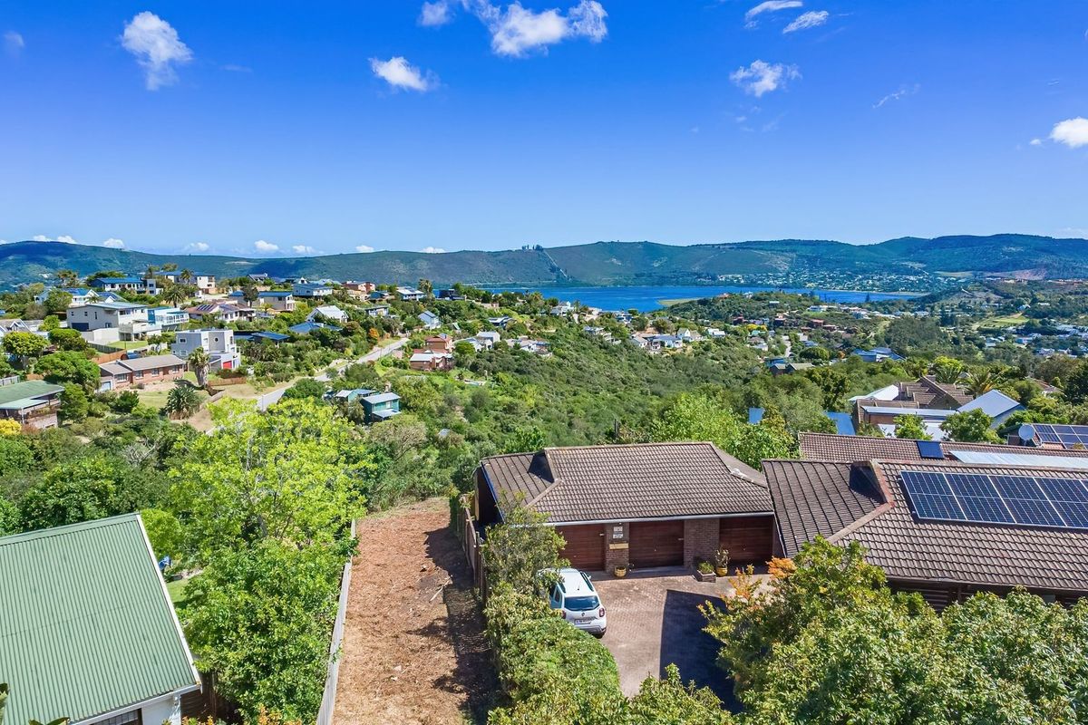 Aerial view of a residential property featuring a tiled roof with solar panels, a paved driveway, and expansive views of the surrounding landscape and lagoon.
