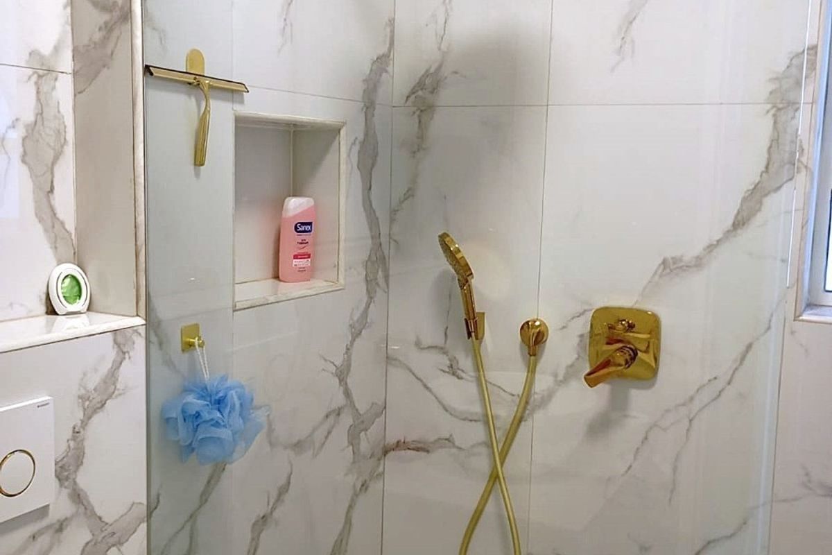 Modern bathroom shower enclosure featuring marble-look wall tiles, mosaic floor tiling, and premium gold-finish fixtures including a rainfall shower head.