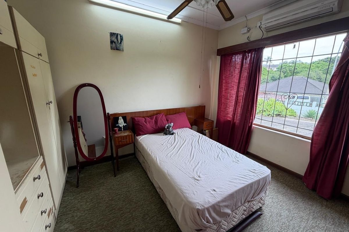 A bedroom featuring built-in cupboards, a ceiling fan, and an air conditioning unit, with security bars installed on the window.