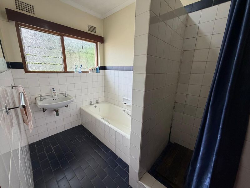 A functional bathroom featuring a built-in bathtub, wall-mounted basin, and a separate tiled shower enclosure with dark floor tiling.