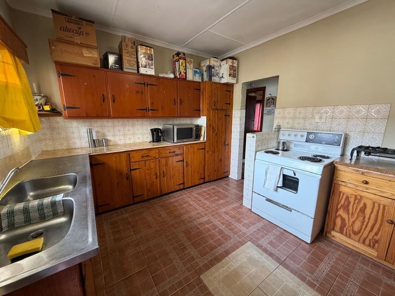 A functional kitchen featuring traditional wooden cabinetry, a double stainless steel sink, tiled backsplash, and a freestanding electric stove.