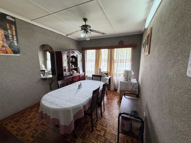 A dining room featuring traditional parquet flooring, a ceiling fan, and textured wall finishes, offering a dated aesthetic ready for modernization.
