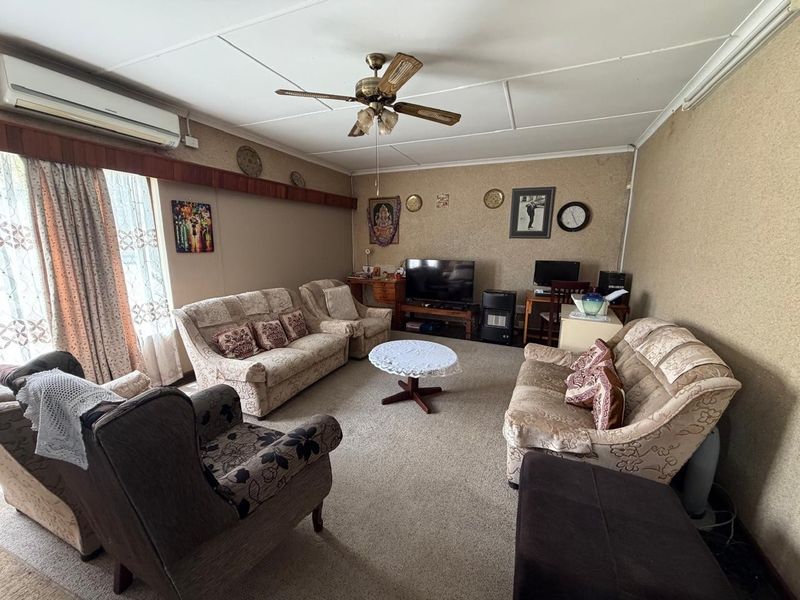 A spacious living room featuring carpeted flooring, a ceiling fan, and a wall-mounted air conditioning unit, offering a comfortable and functional family space.