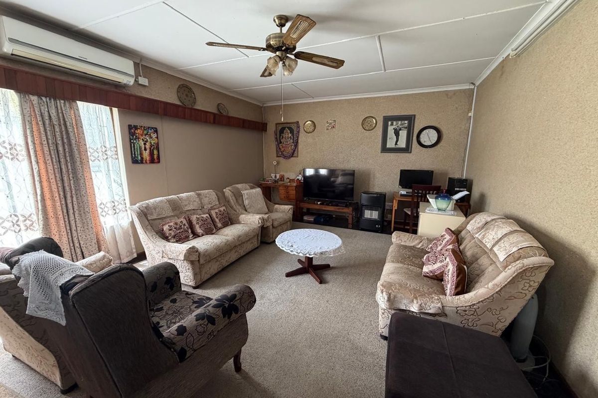A spacious living room featuring carpeted flooring, a ceiling fan, and a wall-mounted air conditioning unit, offering a comfortable and functional family space.