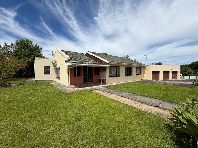 Front view of a single-story house featuring a triple garage, covered patio, tiled roof, and a large front lawn with a paved walkway.