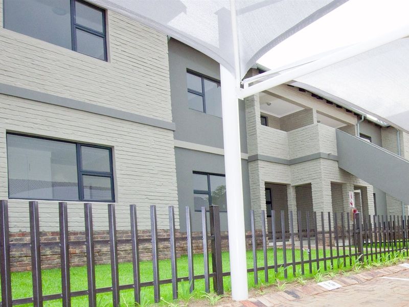Exterior view of a modern apartment complex featuring brick facade, aluminium window frames, and a shaded parking area with perimeter fencing.