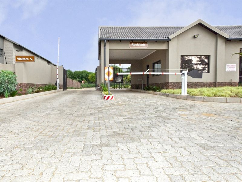 The secure entrance to the apartment complex features a paved driveway, dedicated residents and visitors access lanes, and controlled boom gate security.