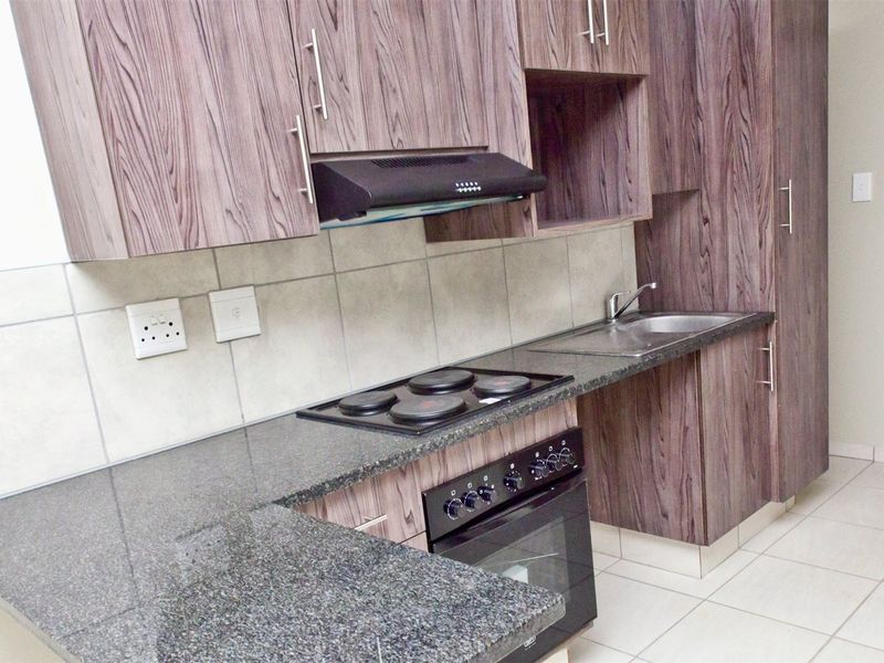 A clean, modern kitchen featuring wood-grain laminate cabinetry, granite countertops, a built-in oven with hob, and a tiled backsplash.