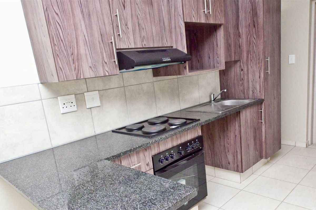 A clean, modern kitchen featuring wood-grain laminate cabinetry, granite countertops, a built-in oven with hob, and a tiled backsplash.