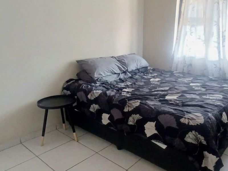 A simple bedroom featuring tiled flooring and a window with curtains, providing a functional and neutral space.