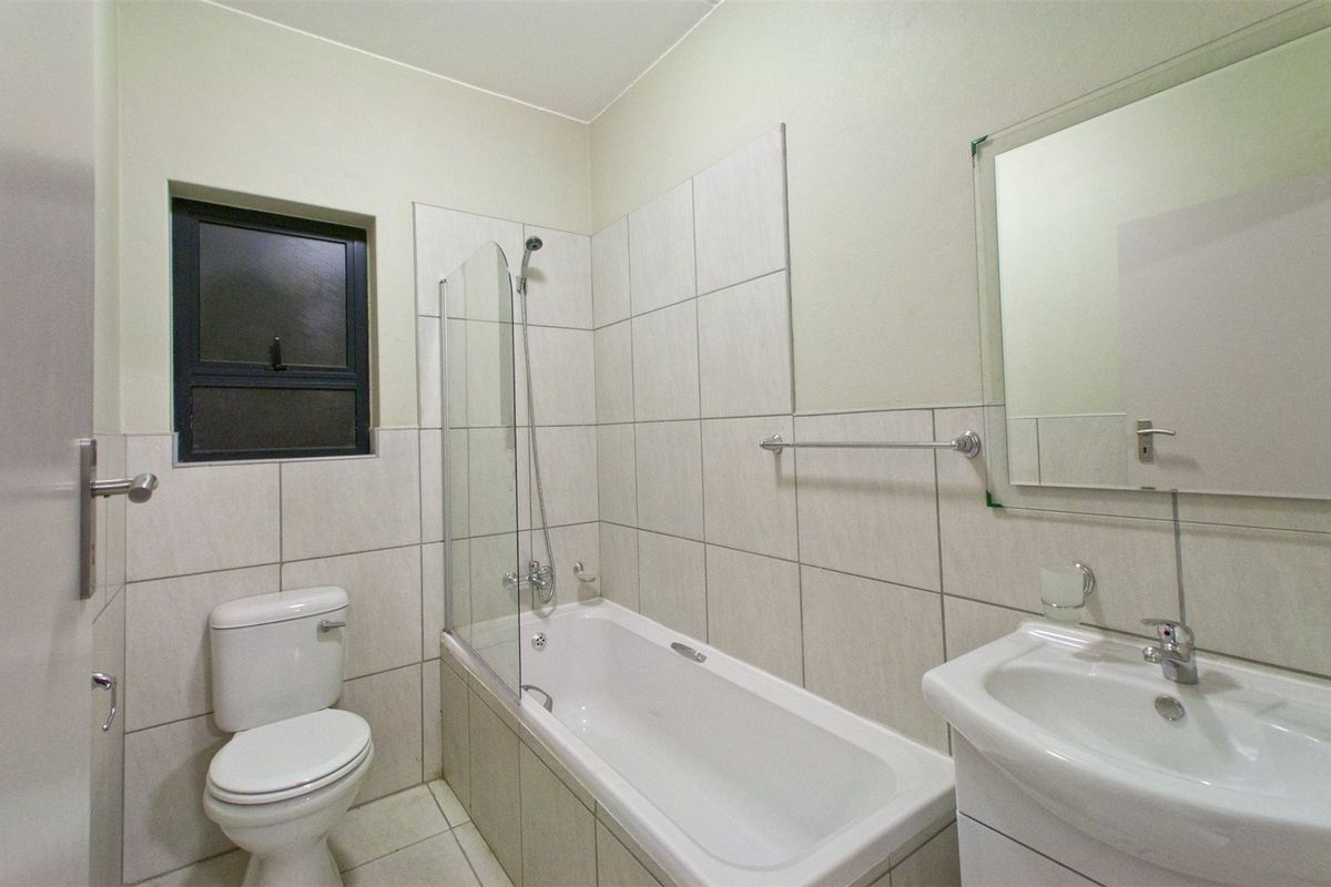 A clean, modern bathroom featuring a bathtub with a glass shower screen, a vanity basin, and neutral wall tiling.