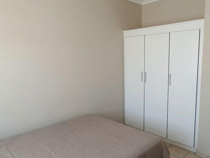 A bedroom featuring neutral wall tones, tiled flooring, and a white built-in wardrobe providing ample storage space.