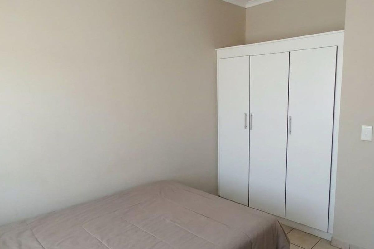 A bedroom featuring neutral wall tones, tiled flooring, and a white built-in wardrobe providing ample storage space.