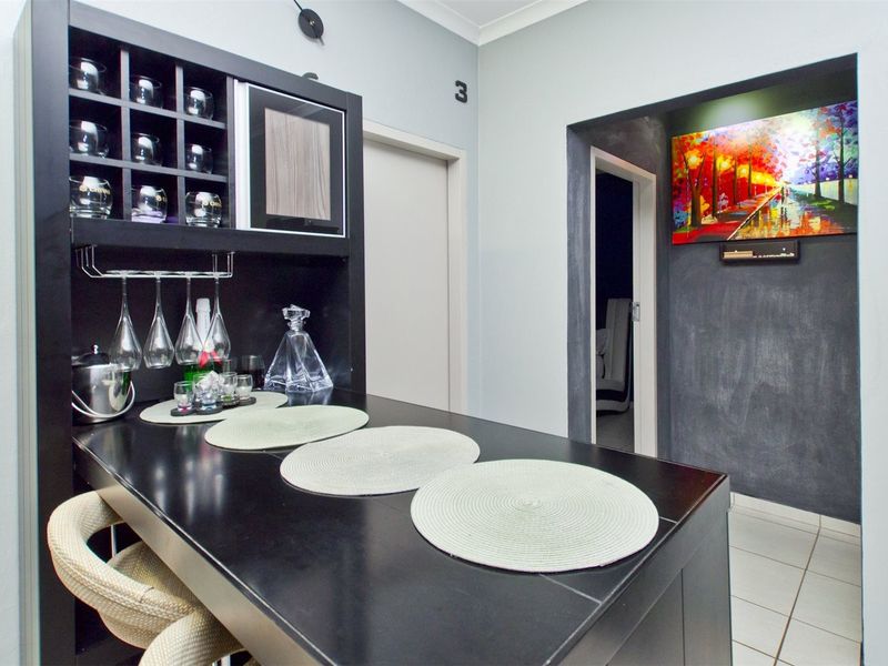 A compact built-in bar area featuring a dark countertop, integrated shelving, and glassware storage, providing a functional space for entertaining.