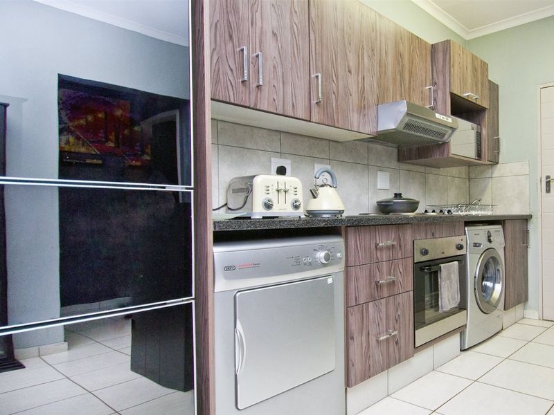 A functional kitchen featuring wood-look laminate cabinetry, stone countertops, a built-in oven, extractor fan, and tiled flooring.