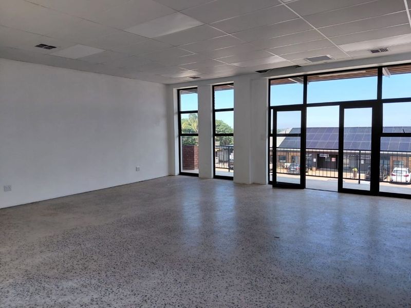 A bright, open-plan office space featuring polished concrete floors, a suspended ceiling, and large windows providing ample natural light and access to a balcony.