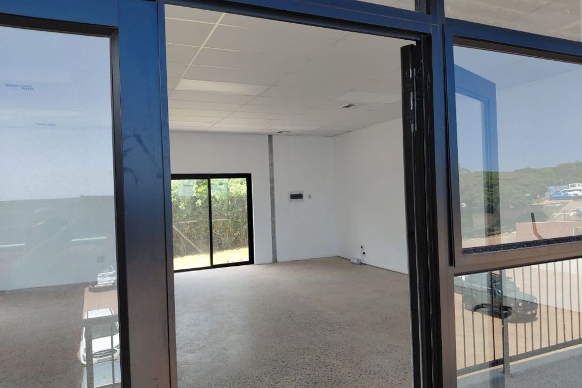 A bright, vacant office space featuring polished concrete floors, a suspended ceiling, and large black aluminium-framed windows providing natural light and exterior views.
