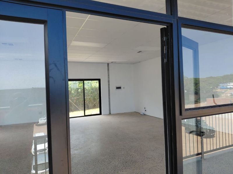 A bright, vacant office space featuring polished concrete floors, a suspended ceiling, and large black aluminium-framed windows providing natural light and exterior views.