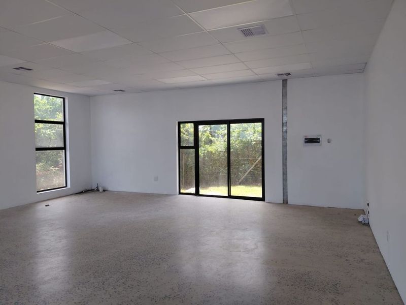 A bright, open-plan office space featuring polished concrete floors, a suspended ceiling, and large windows providing natural light and garden views.