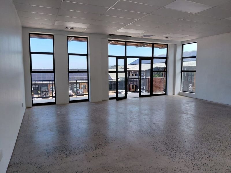 Spacious, empty office area featuring polished concrete floors, suspended ceiling, and large windows providing ample natural light and access to a balcony.