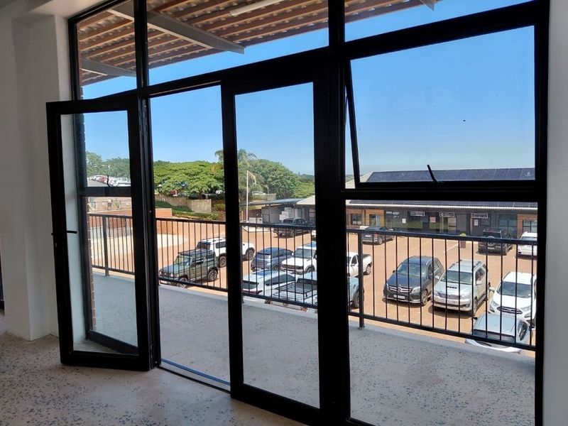 A bright, modern balcony space featuring black aluminium framed glass doors, a metal balustrade, and durable terrazzo flooring overlooking a parking area.
