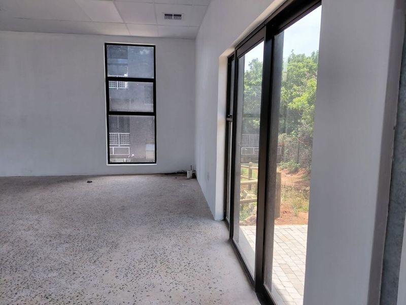 A bright, modern, and empty office space featuring polished concrete floors, large windows, and sliding glass doors leading to an outdoor area.