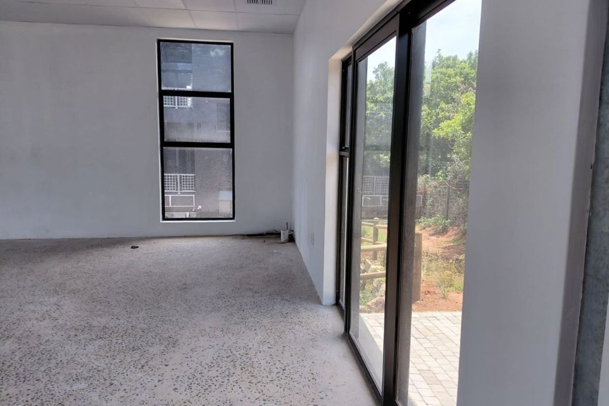 A bright, modern, and empty office space featuring polished concrete floors, large windows, and sliding glass doors leading to an outdoor area.