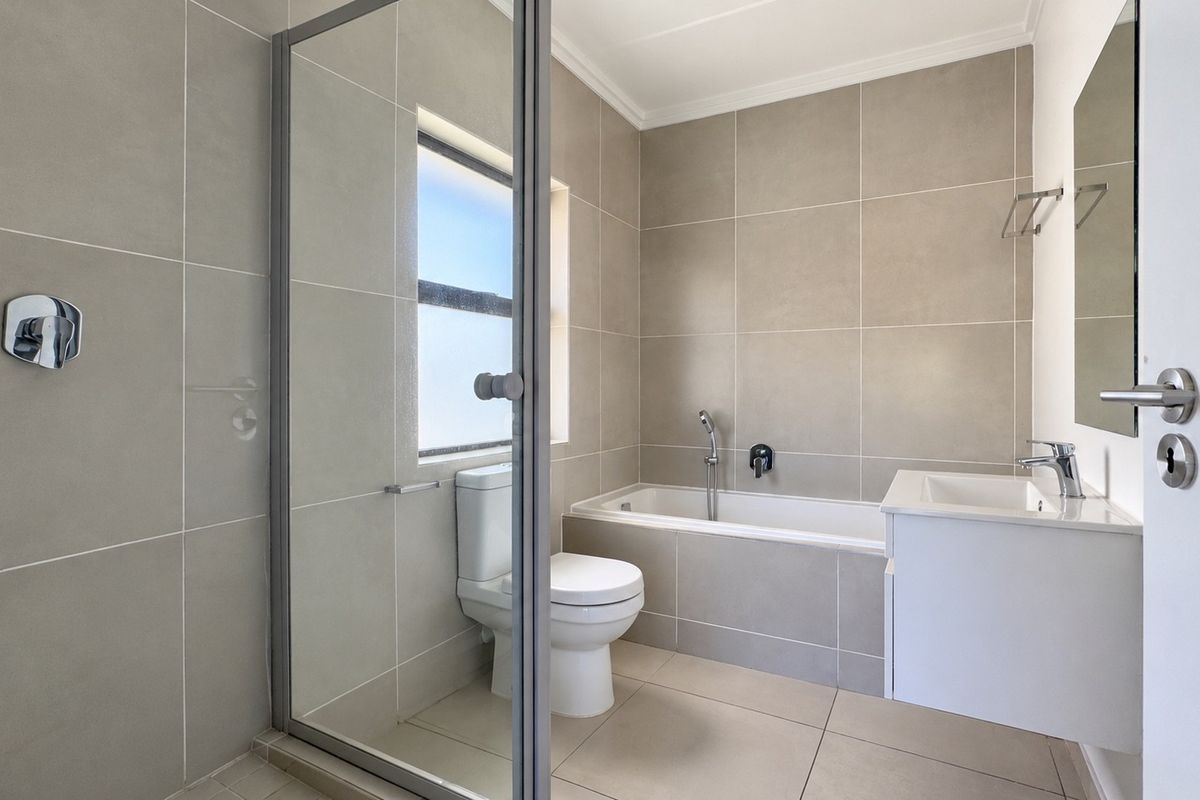 Modern bathroom featuring a glass-enclosed shower, built-in bathtub, wall-mounted vanity, and neutral large-format ceramic tiling throughout.