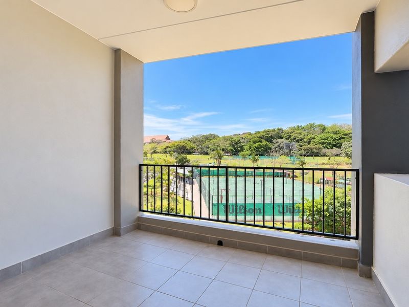A clean, modern covered balcony featuring tiled flooring and a metal balustrade, offering an open view of the surrounding recreational facilities.