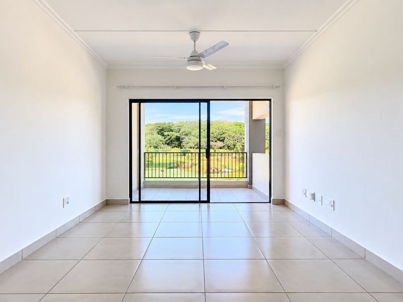 A bright, empty living room featuring neutral tiled flooring, a ceiling fan, and large sliding glass doors that open onto a balcony with scenic views.