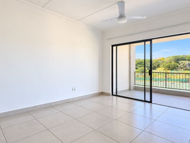 Bright and spacious living area featuring neutral tiled flooring, a ceiling fan, and large sliding glass doors opening onto a private balcony.
