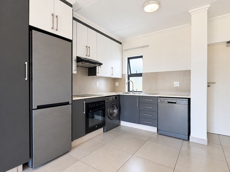 Modern kitchen featuring two-tone cabinetry, integrated oven, extractor fan, stainless steel sink, and tiled flooring with a neutral backsplash.