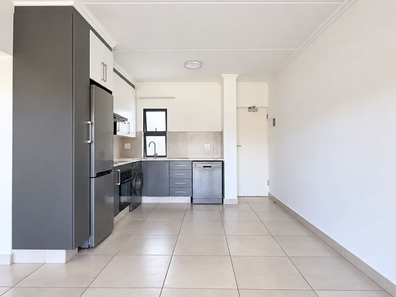 A bright open-plan kitchen and living area featuring modern grey and white cabinetry, tiled flooring, and an adjacent bathroom vanity.