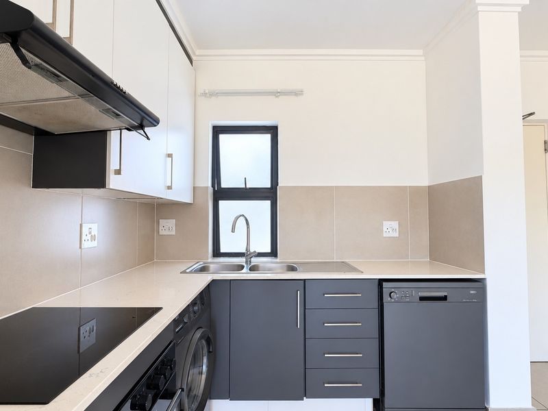 Modern kitchen featuring sleek dark grey cabinetry, stone countertops, integrated appliances, and a stainless steel double sink with a tiled splashback.