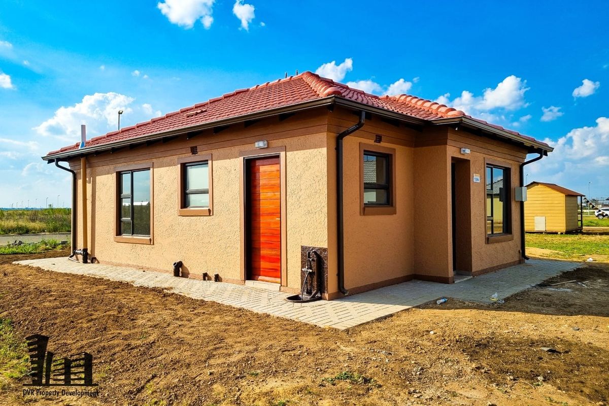 Rear view of a modern single-story house featuring a tiled roof, textured plaster finish, and paved perimeter walkway.