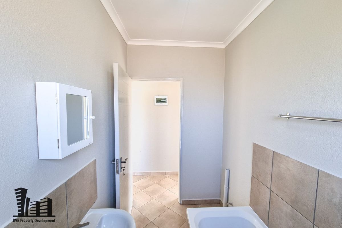 A clean, functional bathroom featuring a basin, bathtub, tiled splashbacks, and neutral floor tiles, presenting a well-maintained and ready-to-use space.