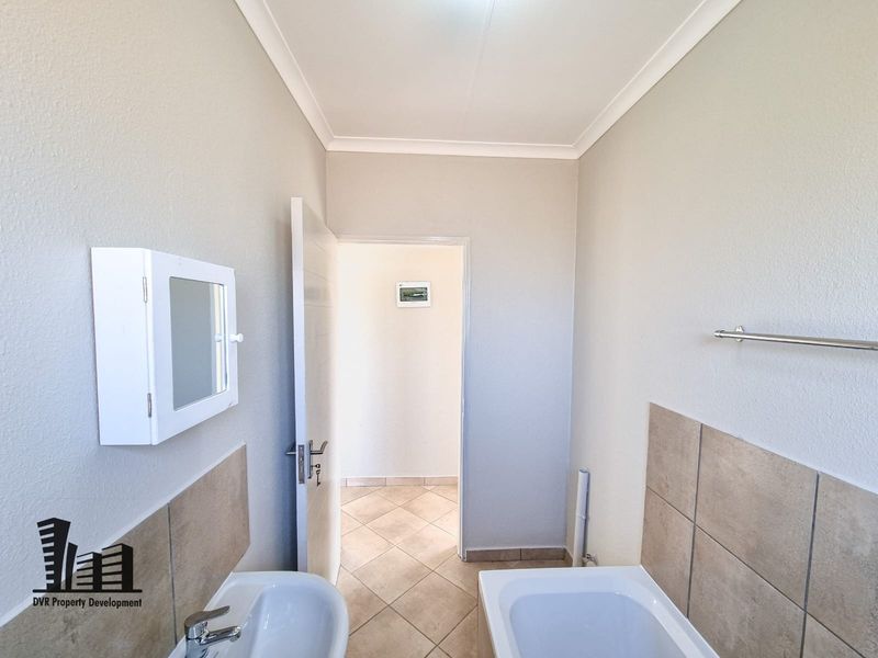 A clean, functional bathroom featuring a basin, bathtub, tiled splashbacks, and neutral floor tiles, presenting a well-maintained and ready-to-use space.