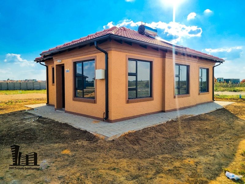 A modern, newly constructed single-story house featuring a tiled roof, solar water heating system, and paved perimeter walkway.