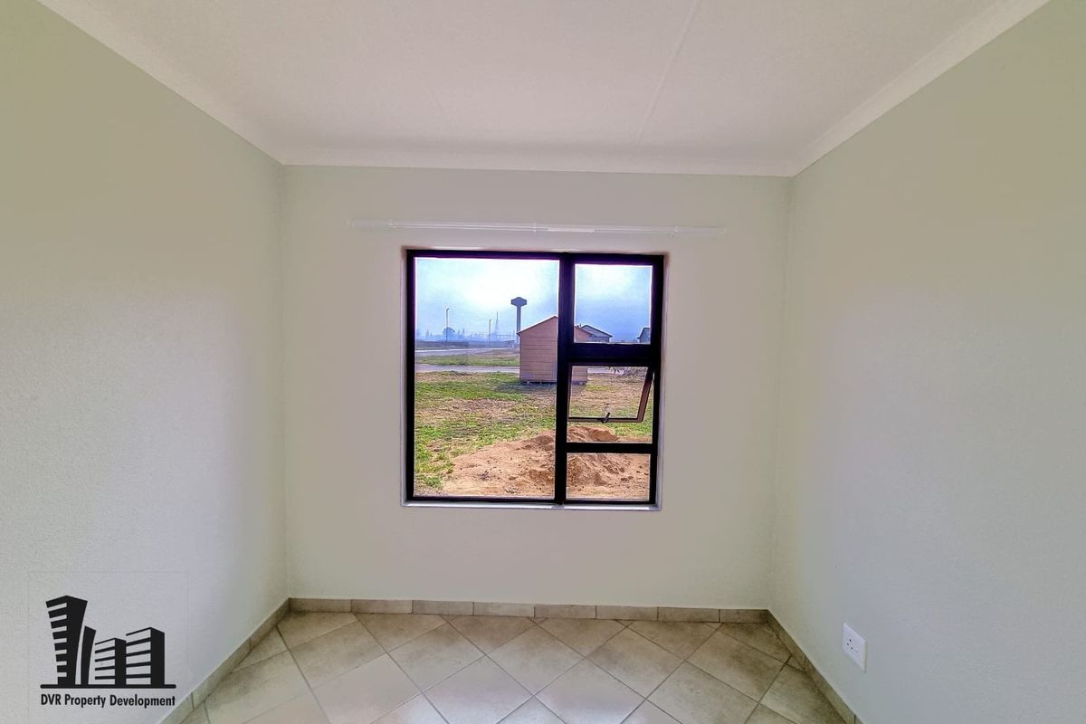 A clean, empty bedroom featuring neutral walls, tiled flooring, and a large aluminium-framed window providing natural light and exterior views.