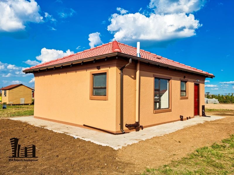 Rear view of a modern single-story house featuring a tiled roof, textured exterior walls, and paved perimeter walkway.