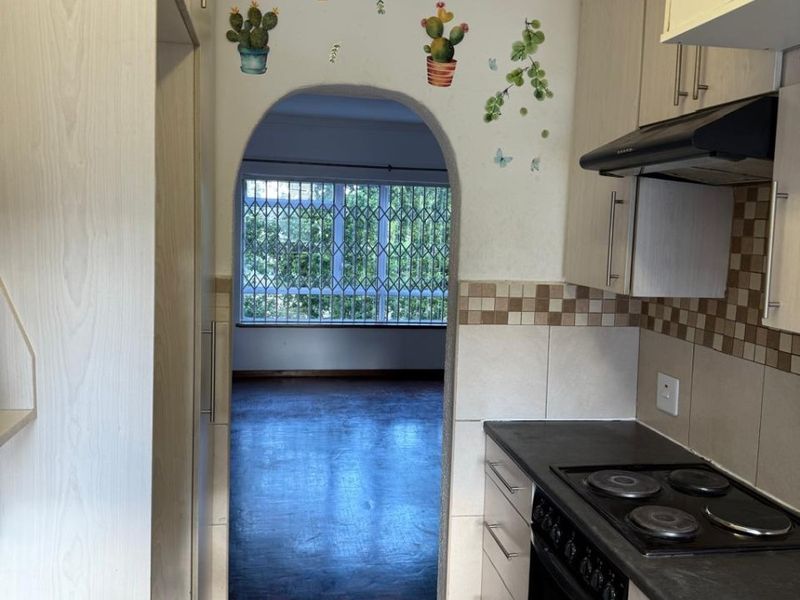 A functional kitchen featuring built-in cabinetry, an electric hob, and an oven, leading through an arched doorway into an adjacent living area.