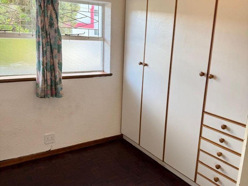 A bedroom featuring built-in cupboards and parquet flooring, offering a functional space with potential for modern updates.
