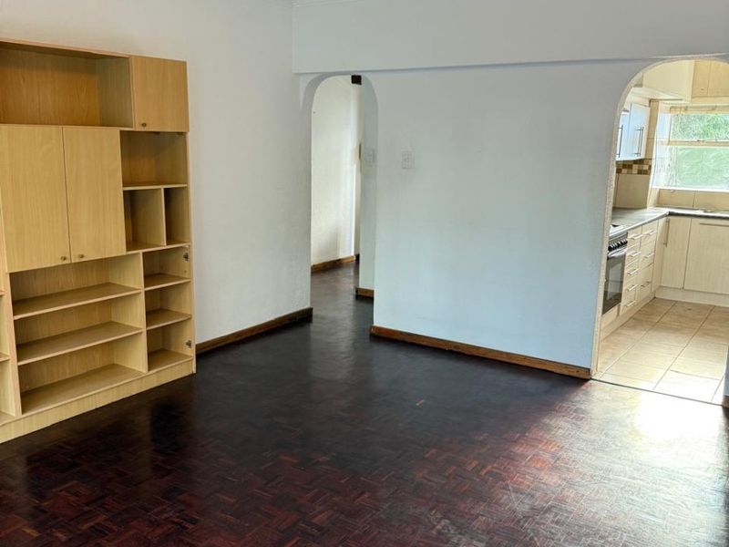 Living area featuring dark parquet flooring and an arched entryway leading to the kitchen, with a built-in shelving unit.