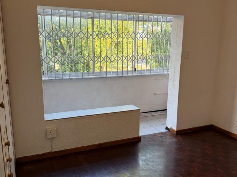 An empty bedroom featuring dark parquet flooring, a built-in wardrobe, and a large window with a security gate overlooking an outdoor balcony area.
