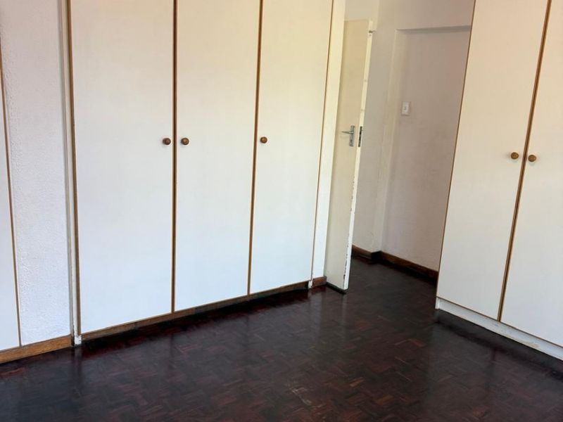 A vacant bedroom featuring classic parquet flooring and extensive built-in cupboard storage, offering a neutral canvas for personalization.